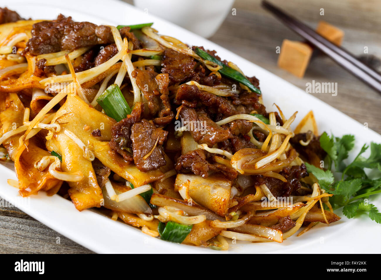 Close up front view of freshly cooked spicy beef, bean sprouts, onion, and tofu with parsley as garnish and chopsticks in holder Stock Photo