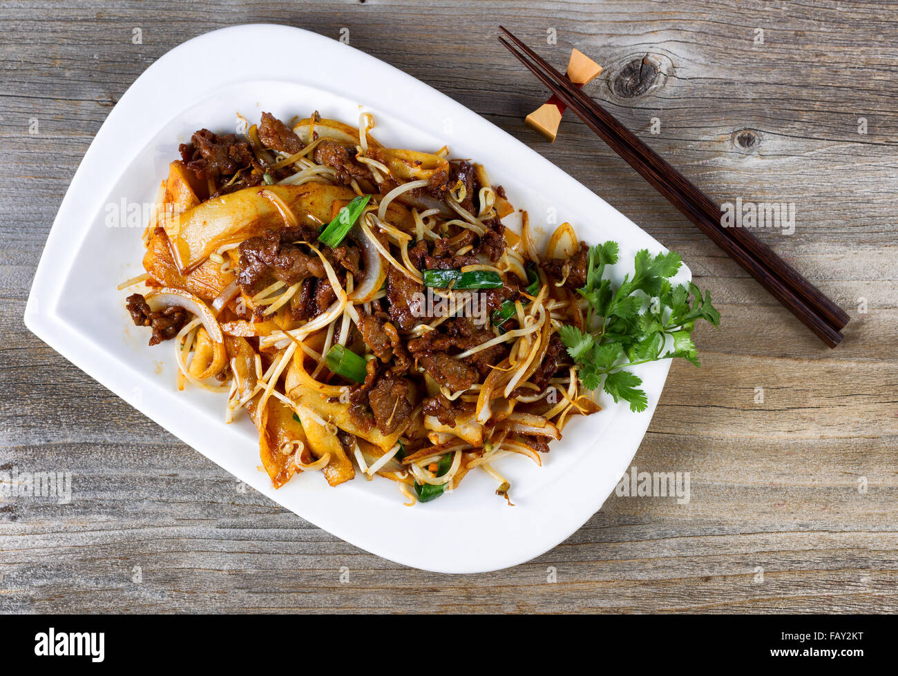 Top view of freshly cooked spicy beef, bean sprouts, onion, tofu with parsley as garnish and chopsticks in holder on rustic wood Stock Photo