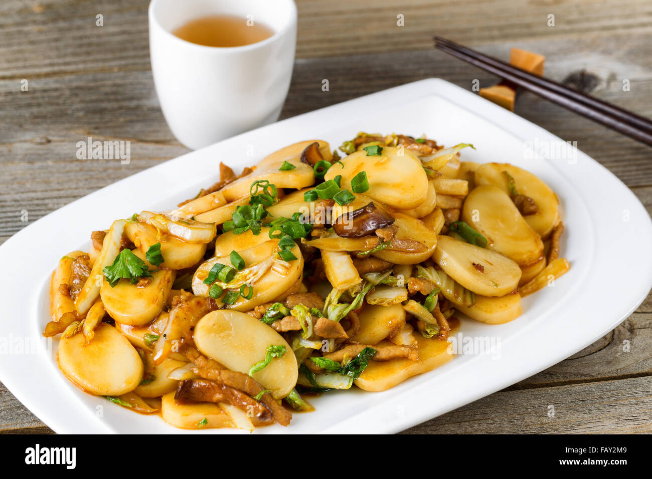Close up front view of stir fry consisting of sliced sticky rice, onion, mushroom, and chicken. Chopsticks and tea in background Stock Photo