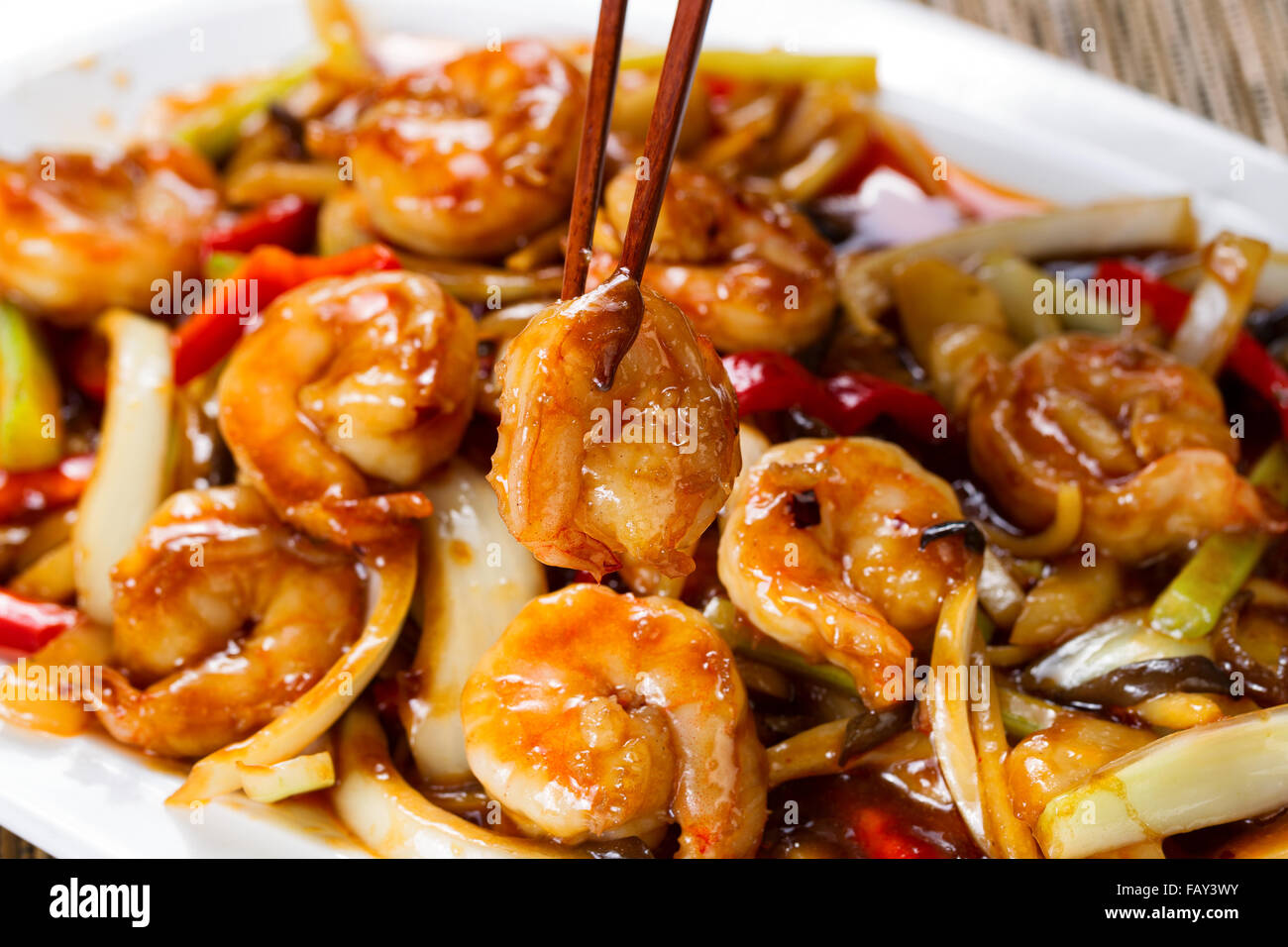 Close up front view of a curry shrimp, selective focus on single piece in chopsticks, with fresh peppers on onion in background. Stock Photo