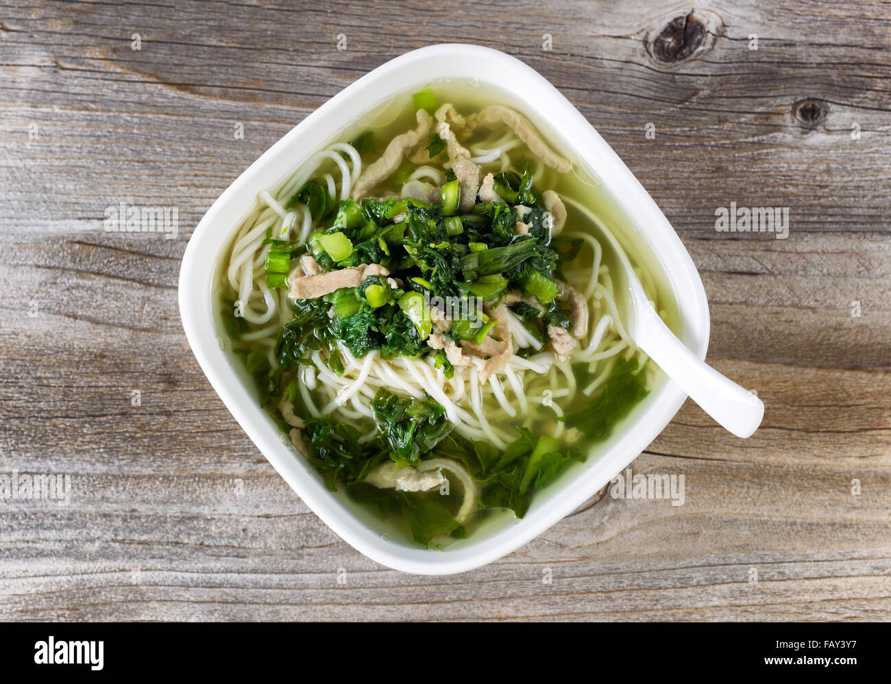 High angled view of noodle and vegetable soup with spoon in bowl on rustic wood. Stock Photo