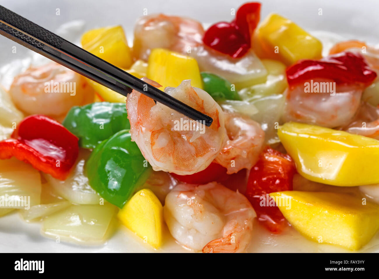 Close up front view of a succulent shrimp, selective focus on single piece in chopsticks, with fresh peppers on onion Stock Photo