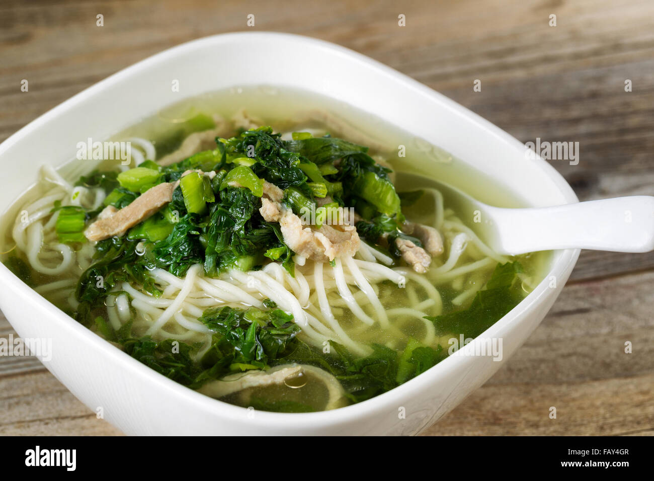 Close up noodle and vegetable soup with spoon in bowl on rustic wood. Stock Photo
