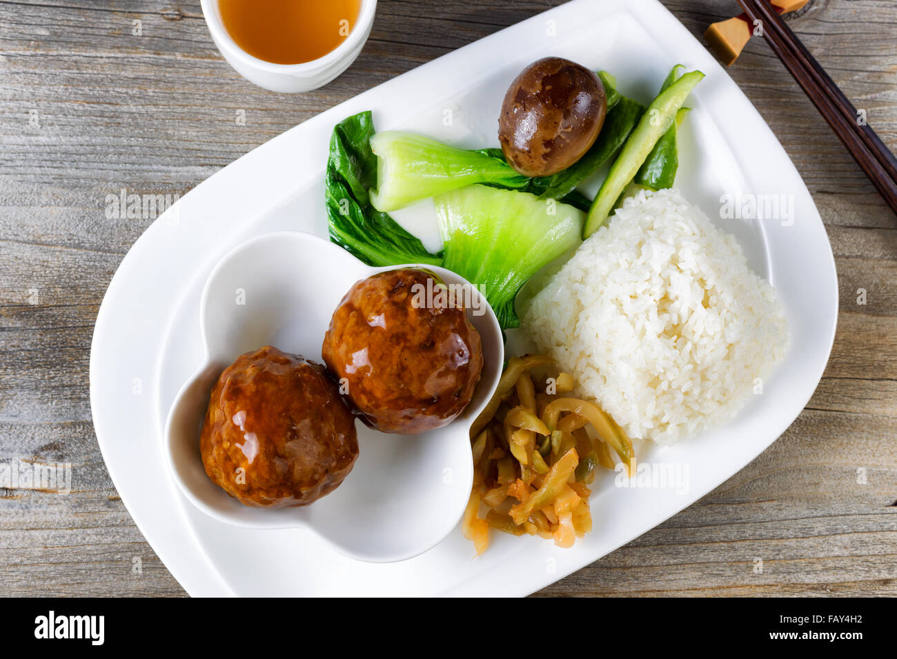 High angled view of Asian saucy meatballs, rice, egg, cucumber and bok choy on white plate. Stock Photo
