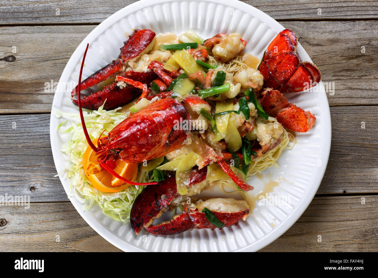 High angled view freshly cooked whole Maine lobster covered with herbs, onions, and sauce on white plate. Stock Photo