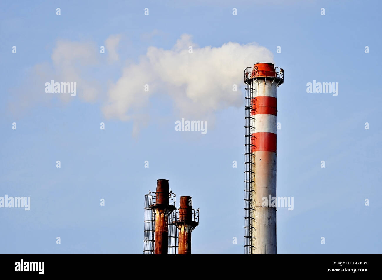 Smoke and steam coming out from an industrial petrochemical plant chimney with a blue sky on the background Stock Photo