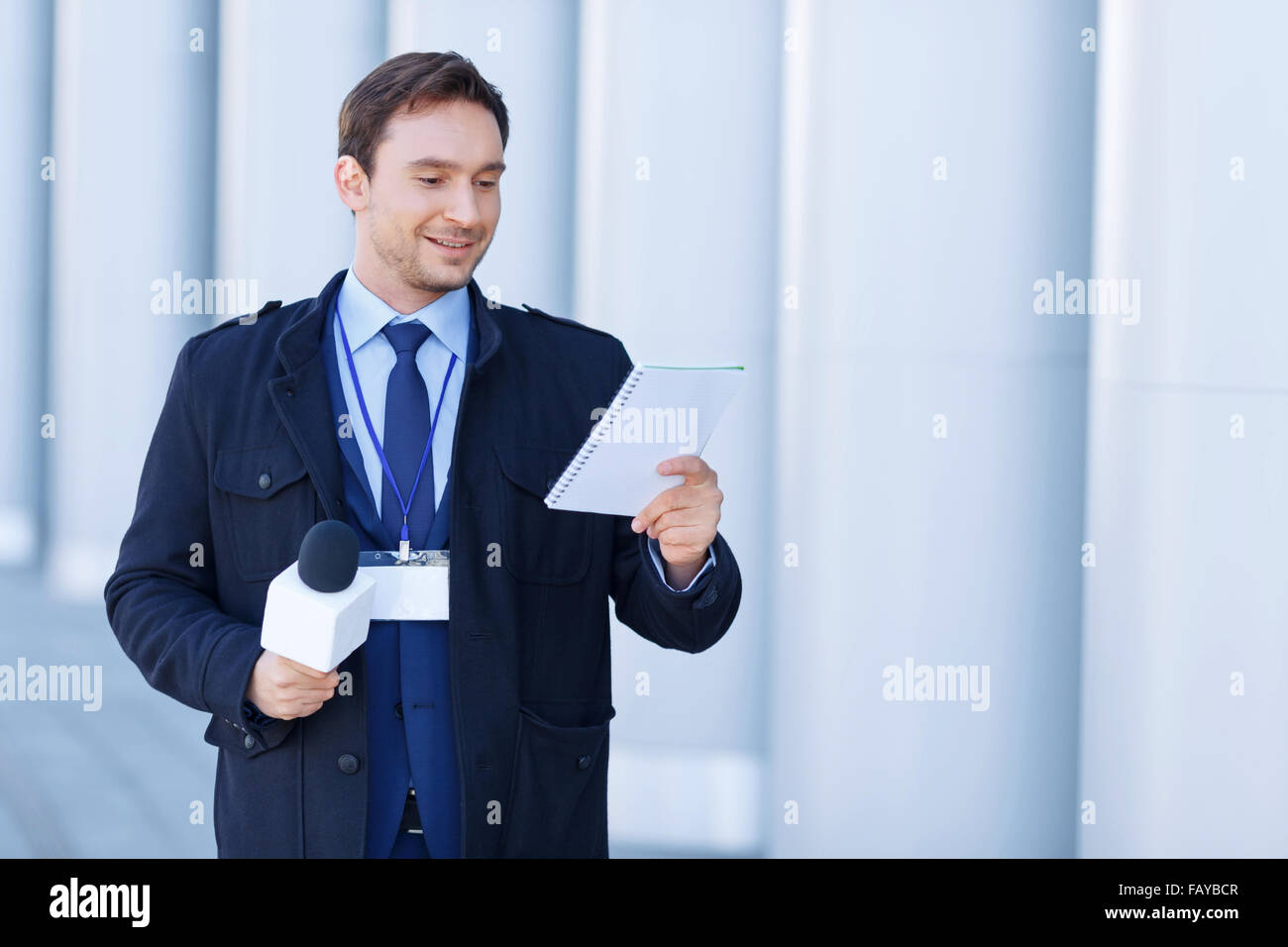 Newsman looks into his notepad while holding the microphone. Stock Photo