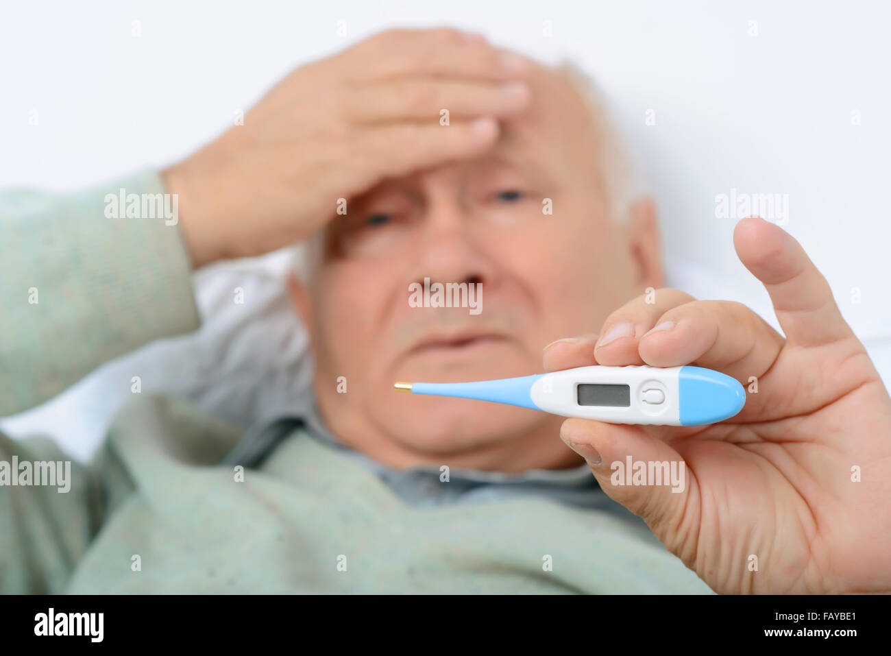 Tired man clutches at his forehead showing the thermometer. Stock Photo