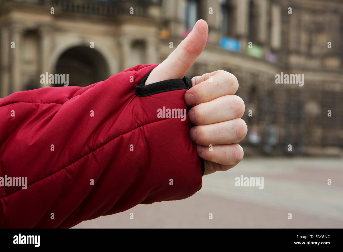 A man makes a thumbs up gesture. His thumb pokes through the wrist loop of a red jacket. Stock Photo