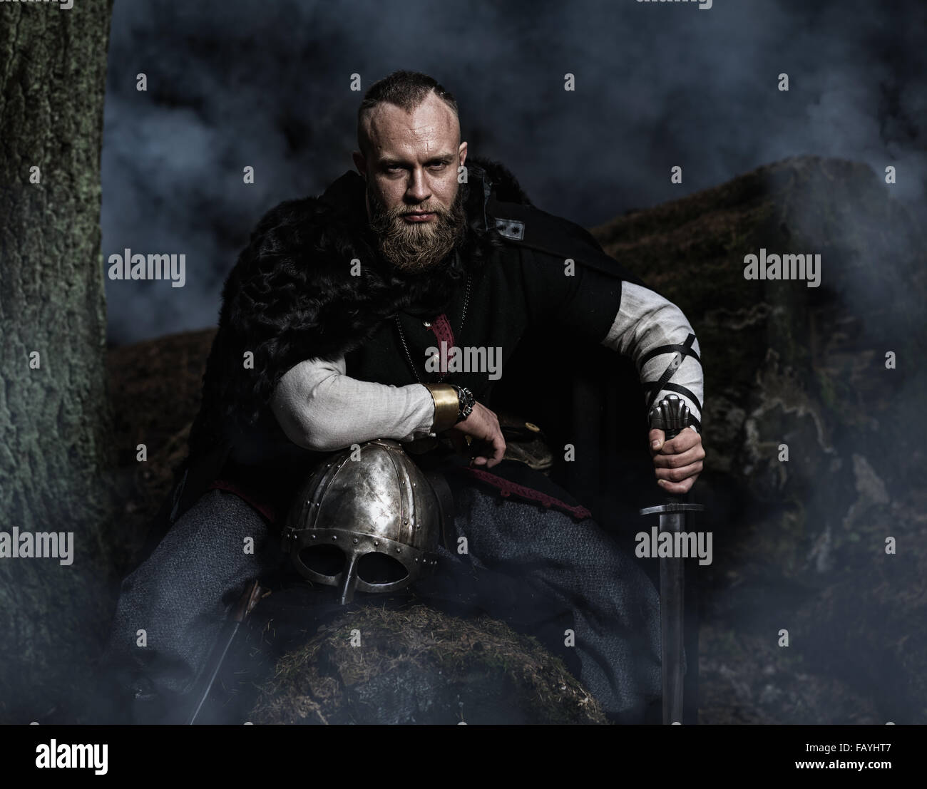 Viking with sword and helmet on a background of smoky forest. Warrior resting. Historic costume. Stock Photo