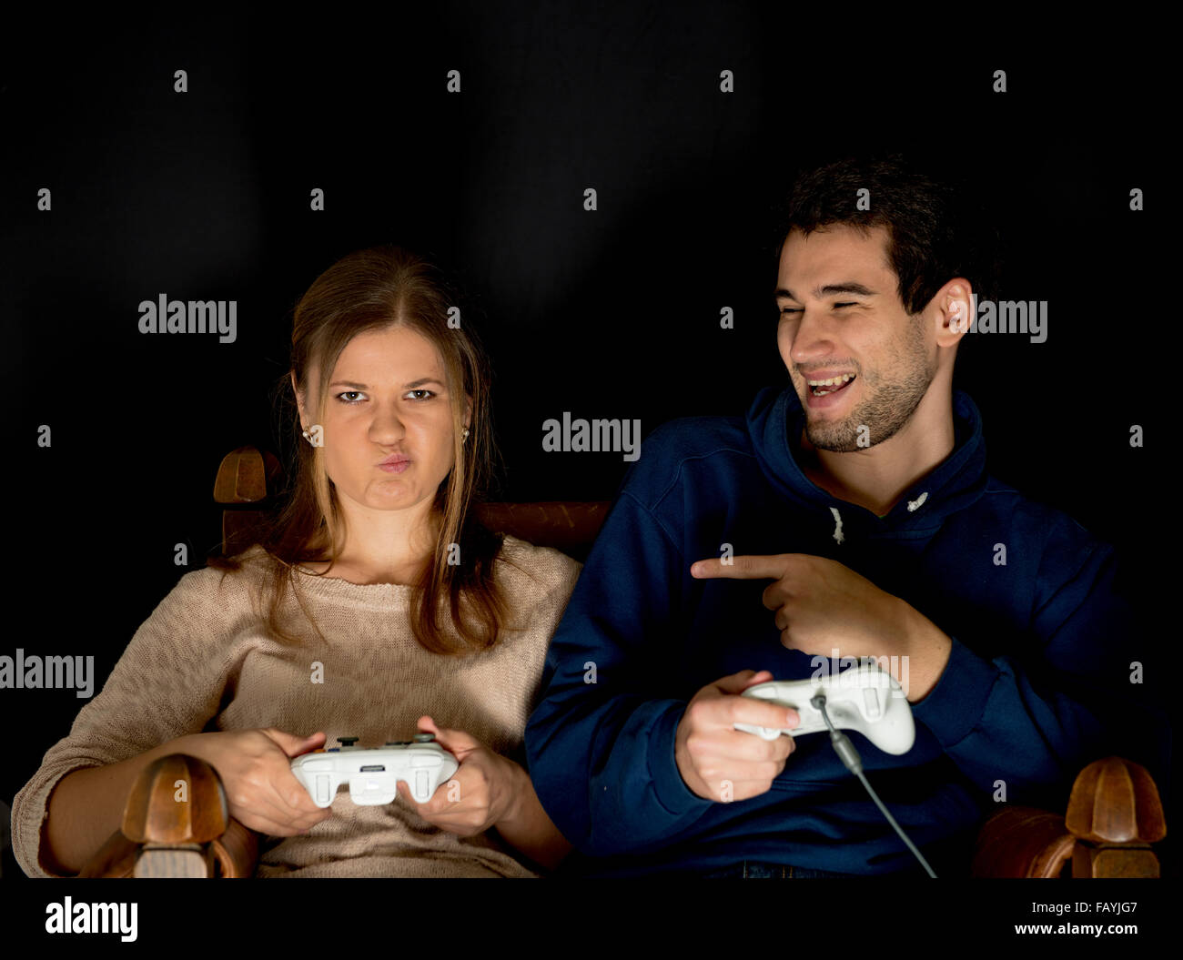 Young couple, man and woman play computer games sitting in dark room in front of tv or monitor, holding game controllers in thei Stock Photo