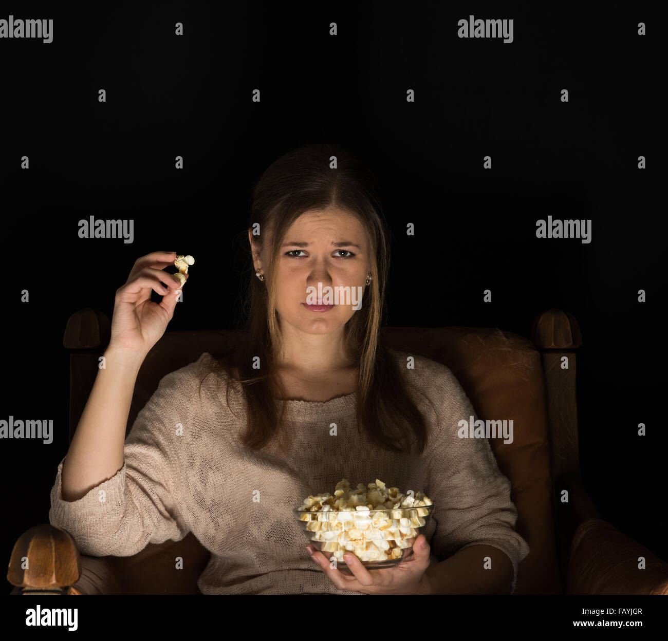 young  woman, sitting in the dark room in the front of tv watching movie and eating popcorn, showing emotions. Stock Photo
