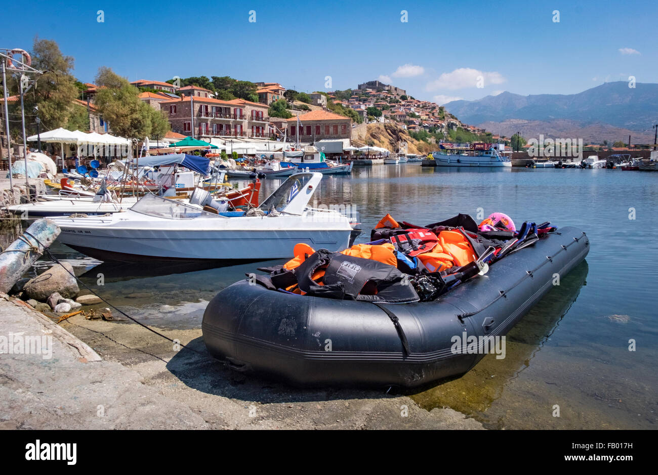 Rescued refugee raft/dinghy filled with life vests and tied up in Molyvos harbor next to pleasure boats. Stock Photo
