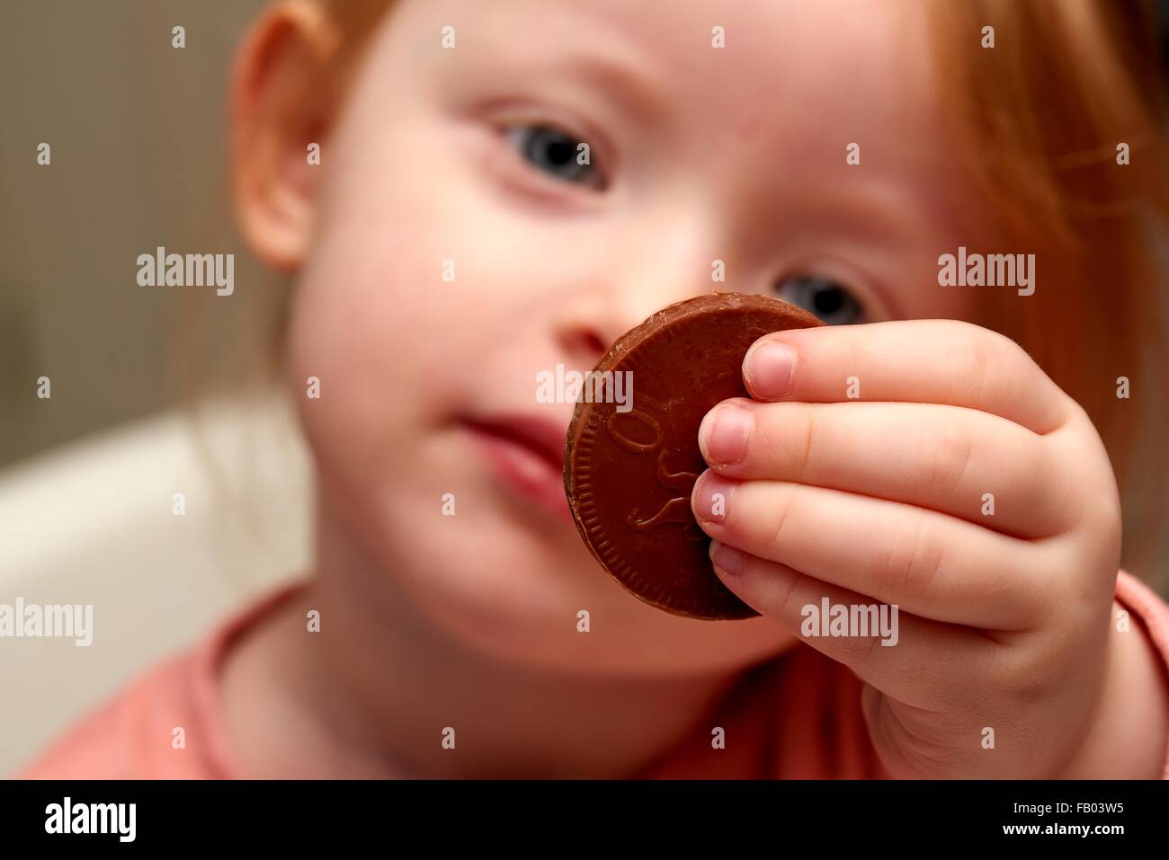 A three year old girl holding a chocolate coin Stock Photo