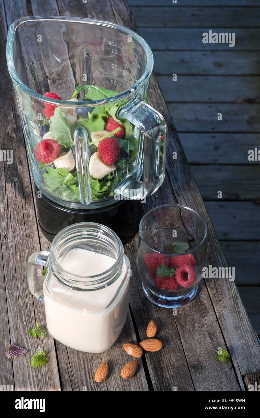 Blender with healthy smoothie ingredients - almond milk, fresh fruit, baby kale - on rustic wood table. Stock Photo