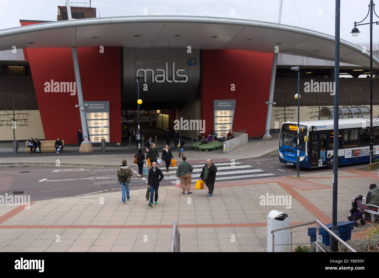 'The Malls' in Basingstoke as viewed from outside the train station and pedestrians crossing a zebra crossing in front of a bus. England, UK Stock Photo