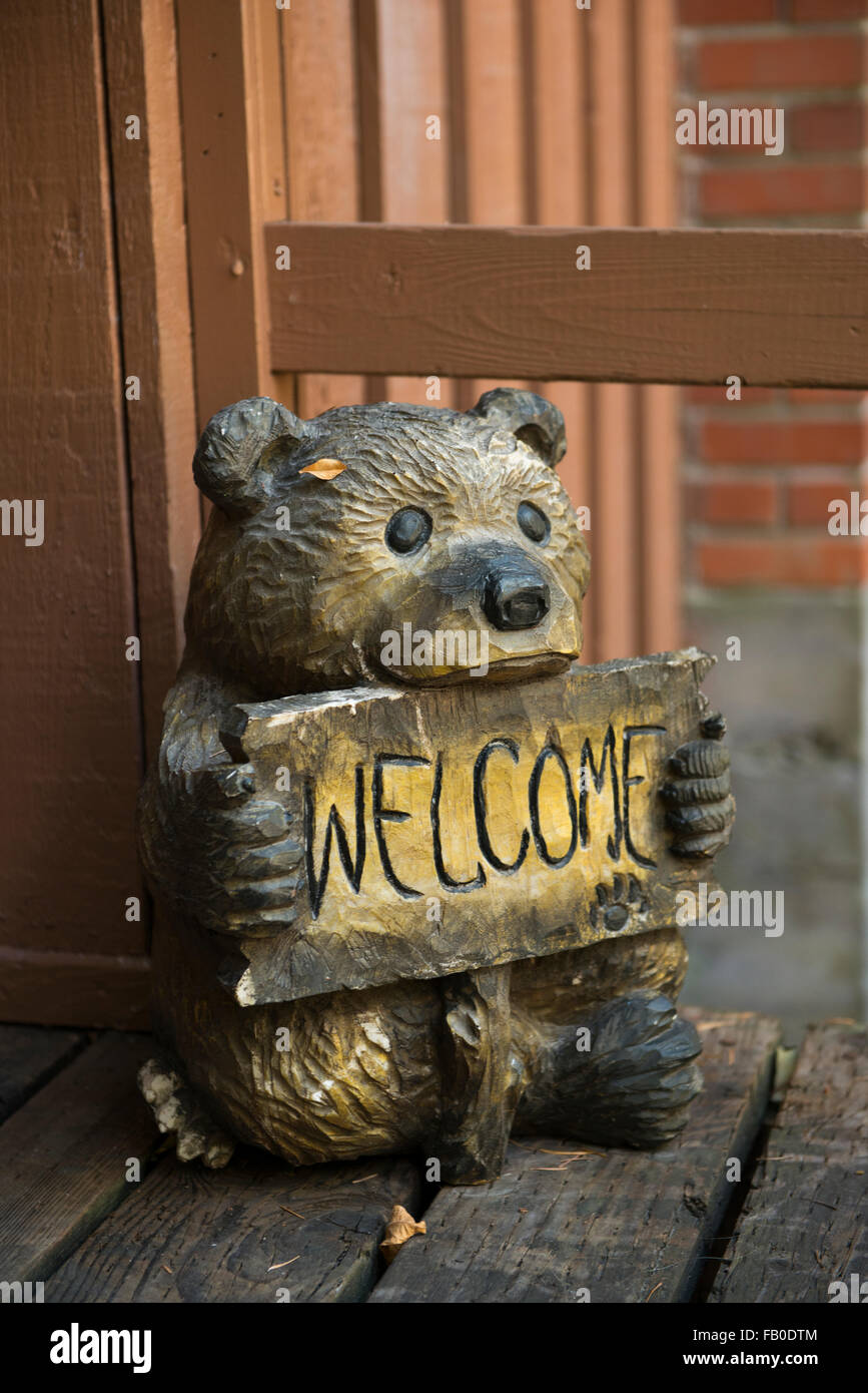 A carved wooden bear holds a welcome sign at Heaven's Gate River Cottages, vacation rentals located along the McKenzie River. Stock Photo