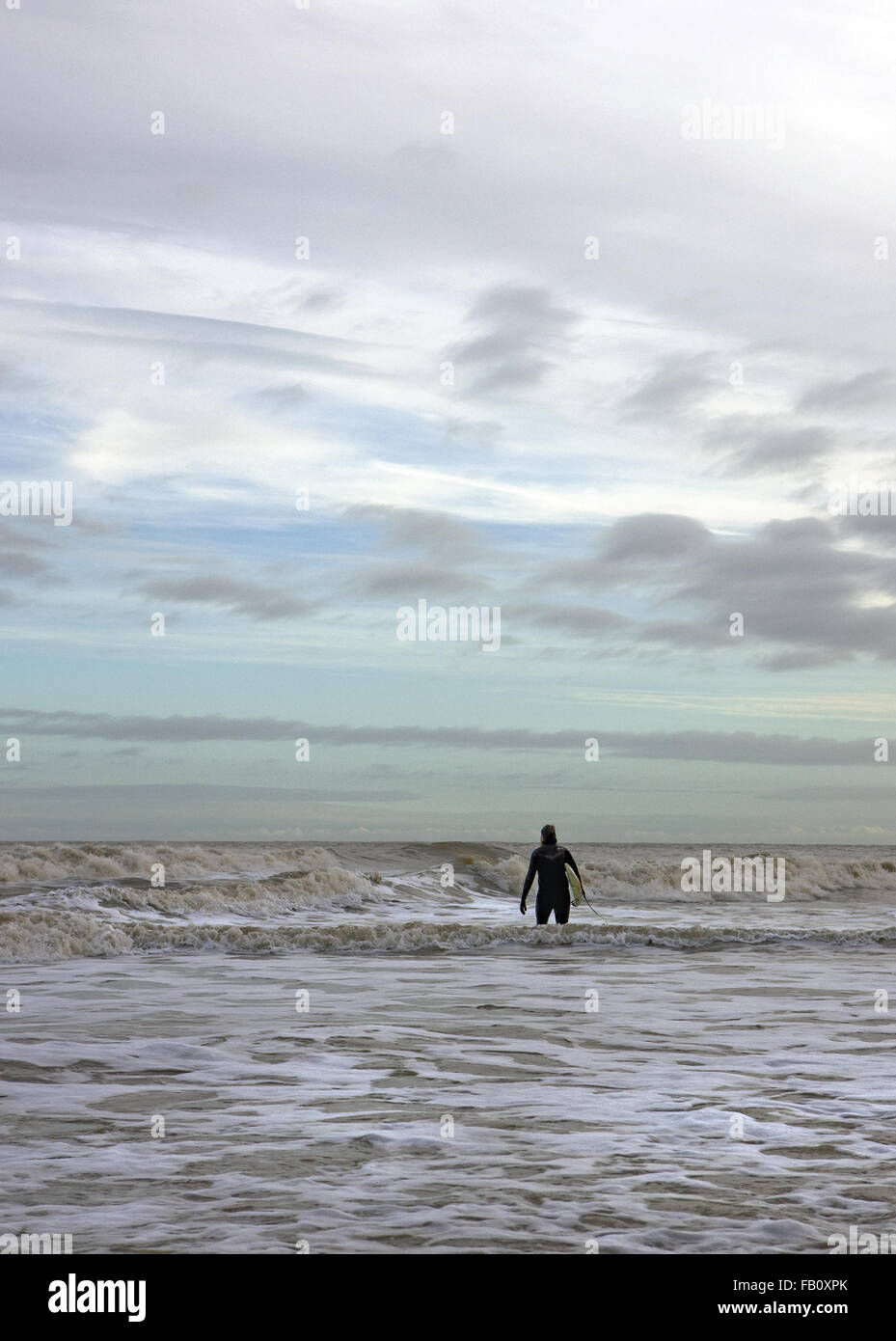 Surfer silhouetted walking through the surf in a winter sea Stock Photo