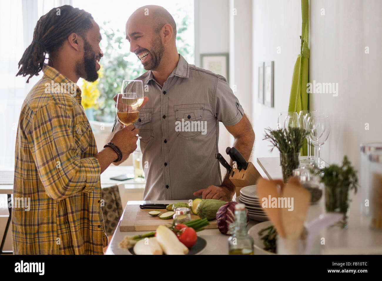 Smiley homosexual couple drinking wine in kitchen Stock Photo