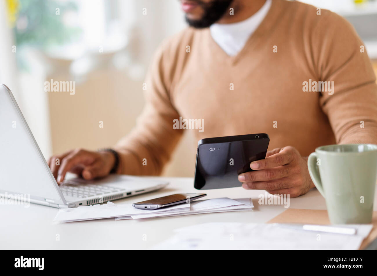 Man working with laptop at table and holding digital tablet Stock Photo