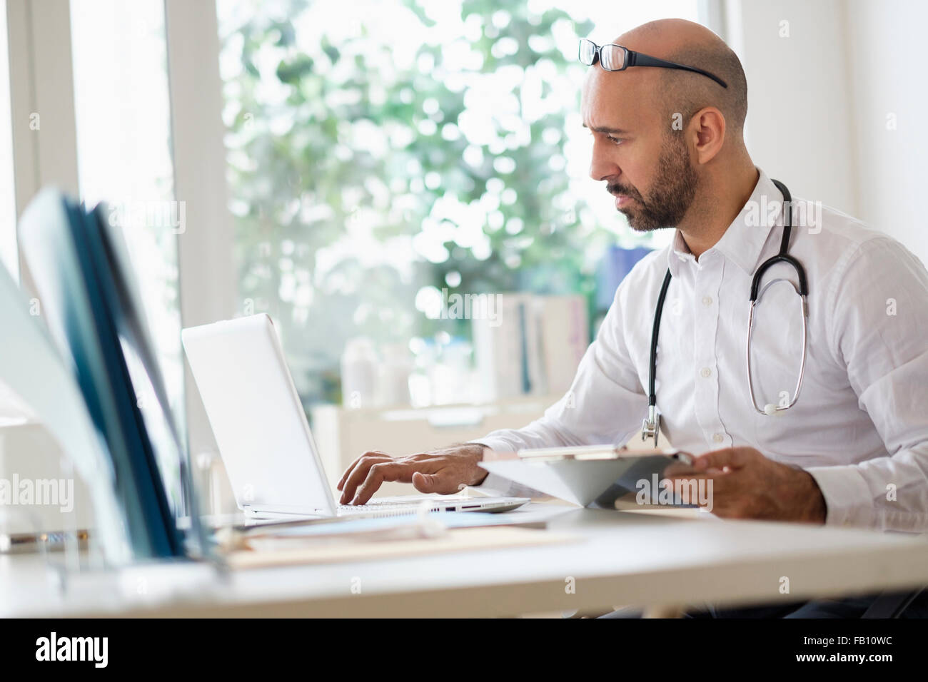 Concentrated doctor working with laptop at desk in office Stock Photo