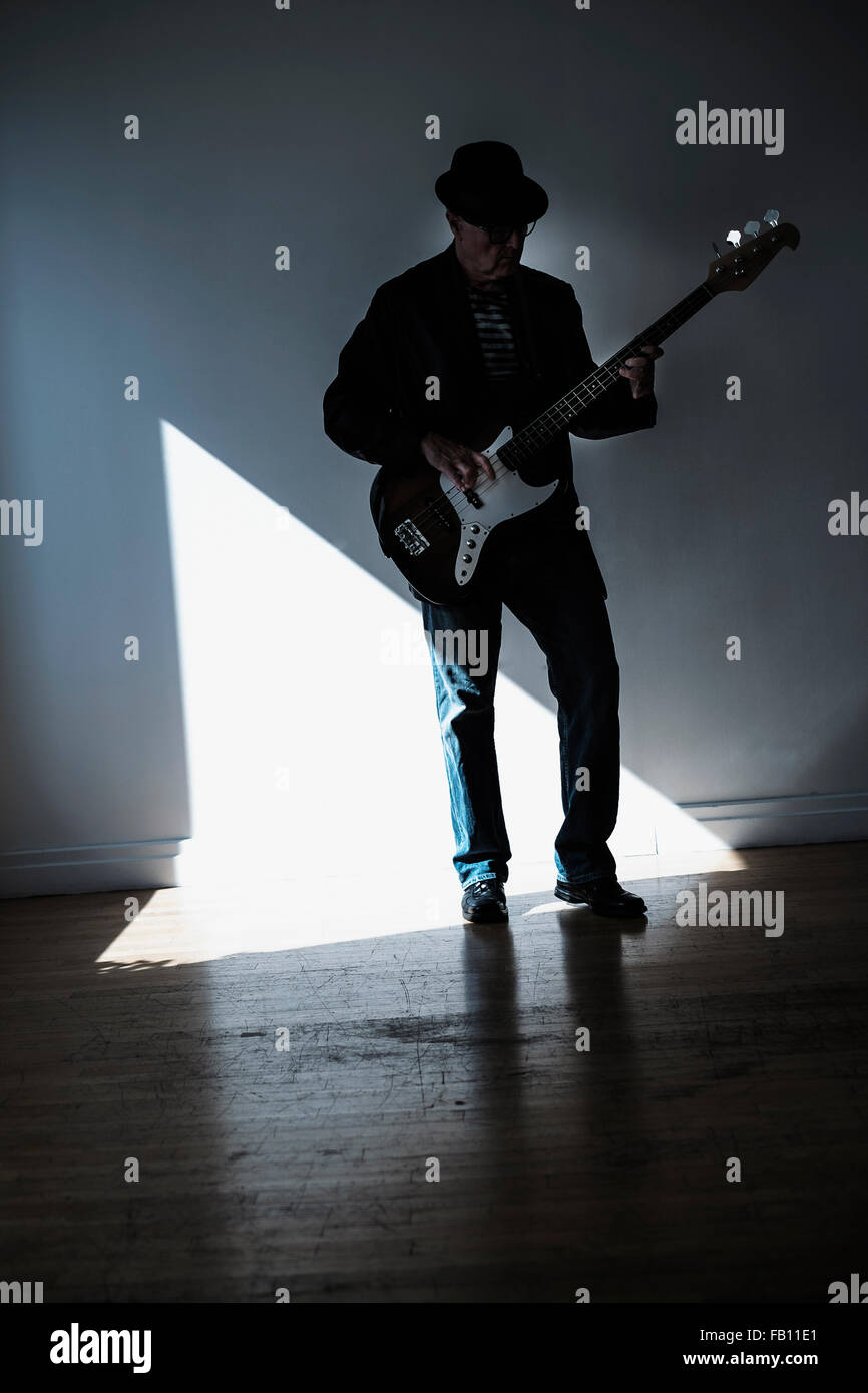 Man playing bass guitar in empty room Stock Photo