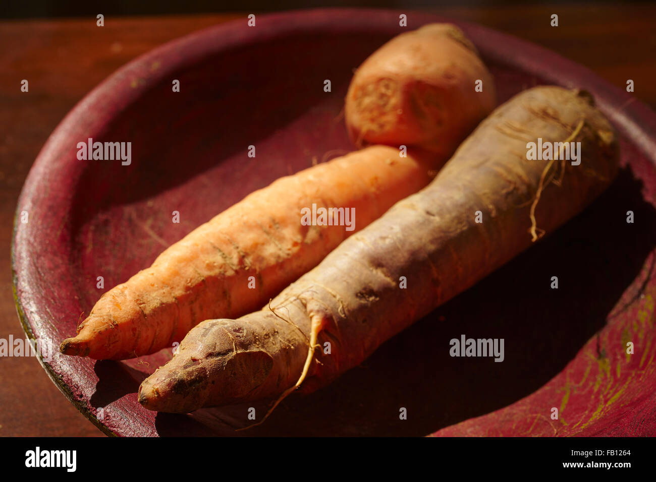 ugly carrots in a red wooden bowl Stock Photo
