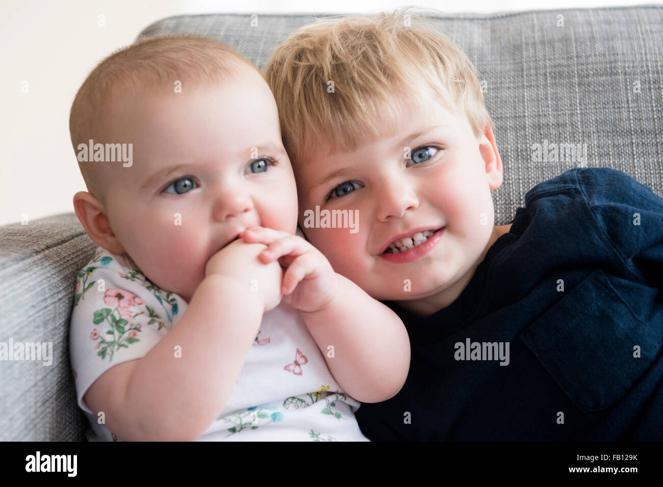 Boy (2-3) with baby sister (12-17 months) sitting on sofa Stock Photo