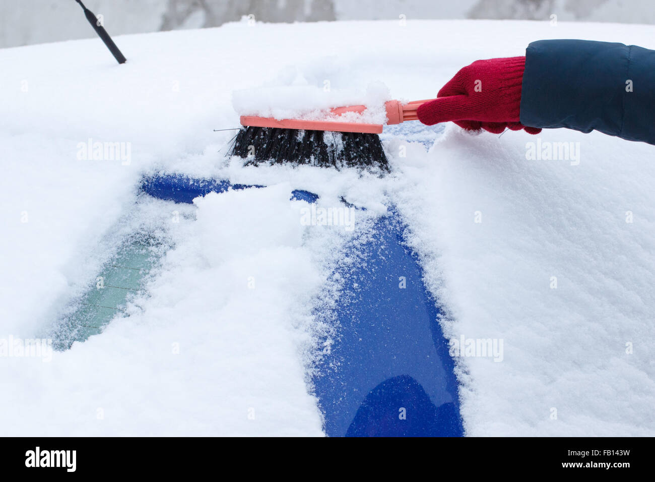 Hand of woman using brush and remove snow and ice from car and