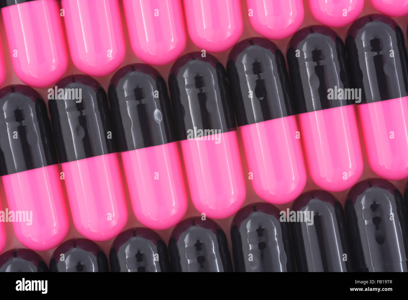 Close-up of pills - capsule form made of gelatin. Pink / Black pills. Metaphor taking on American drug companies over high drug prices, drug trials. Stock Photo