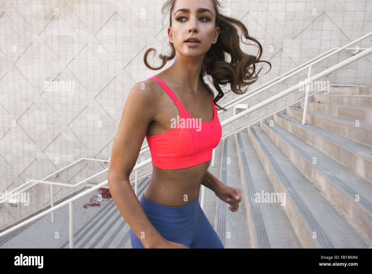 Young woman wearing sports bra running up stairs, looking away Stock Photo
