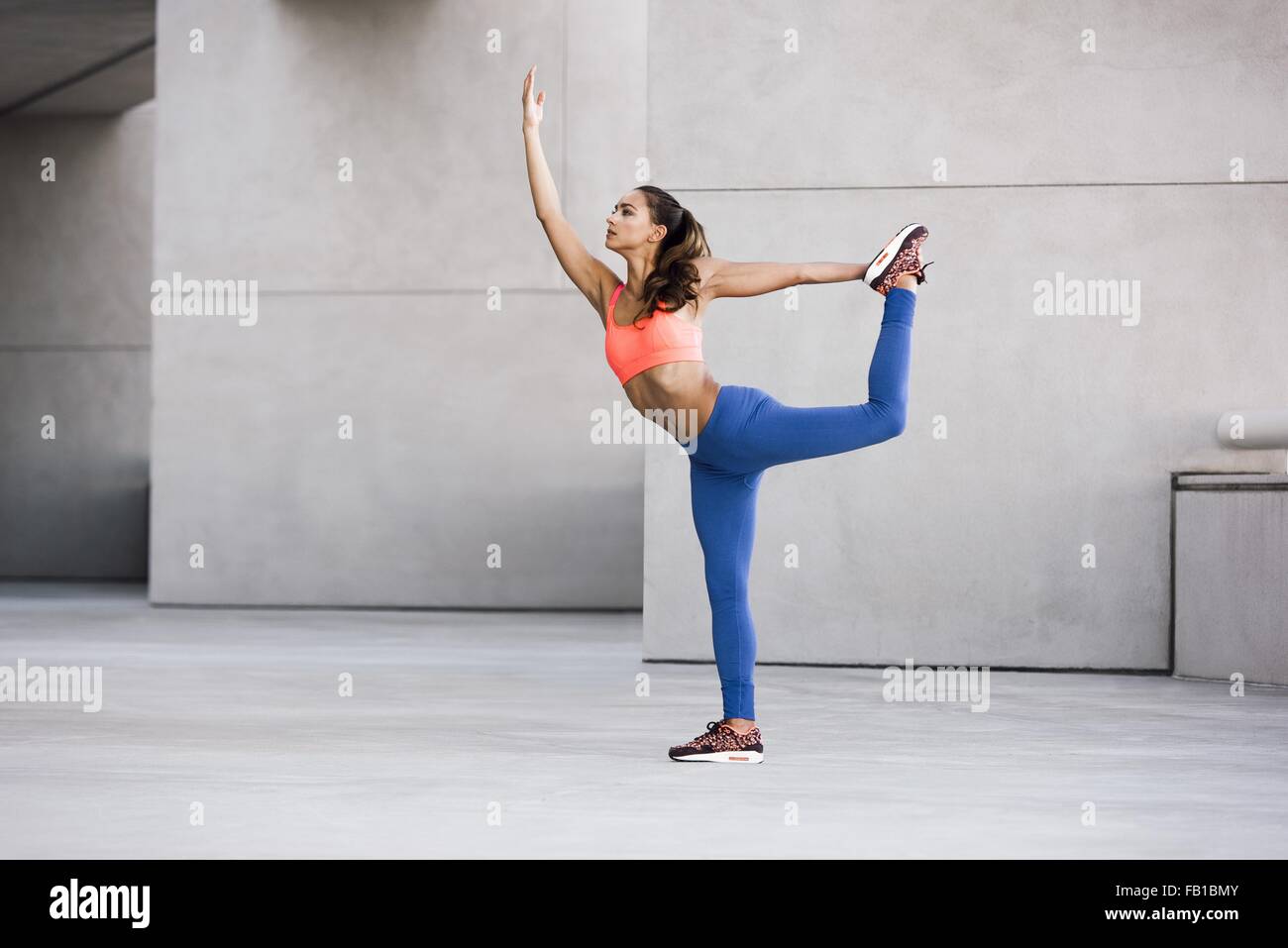 Side view of young woman balancing on one leg, leg raised holding ankle stretching Stock Photo