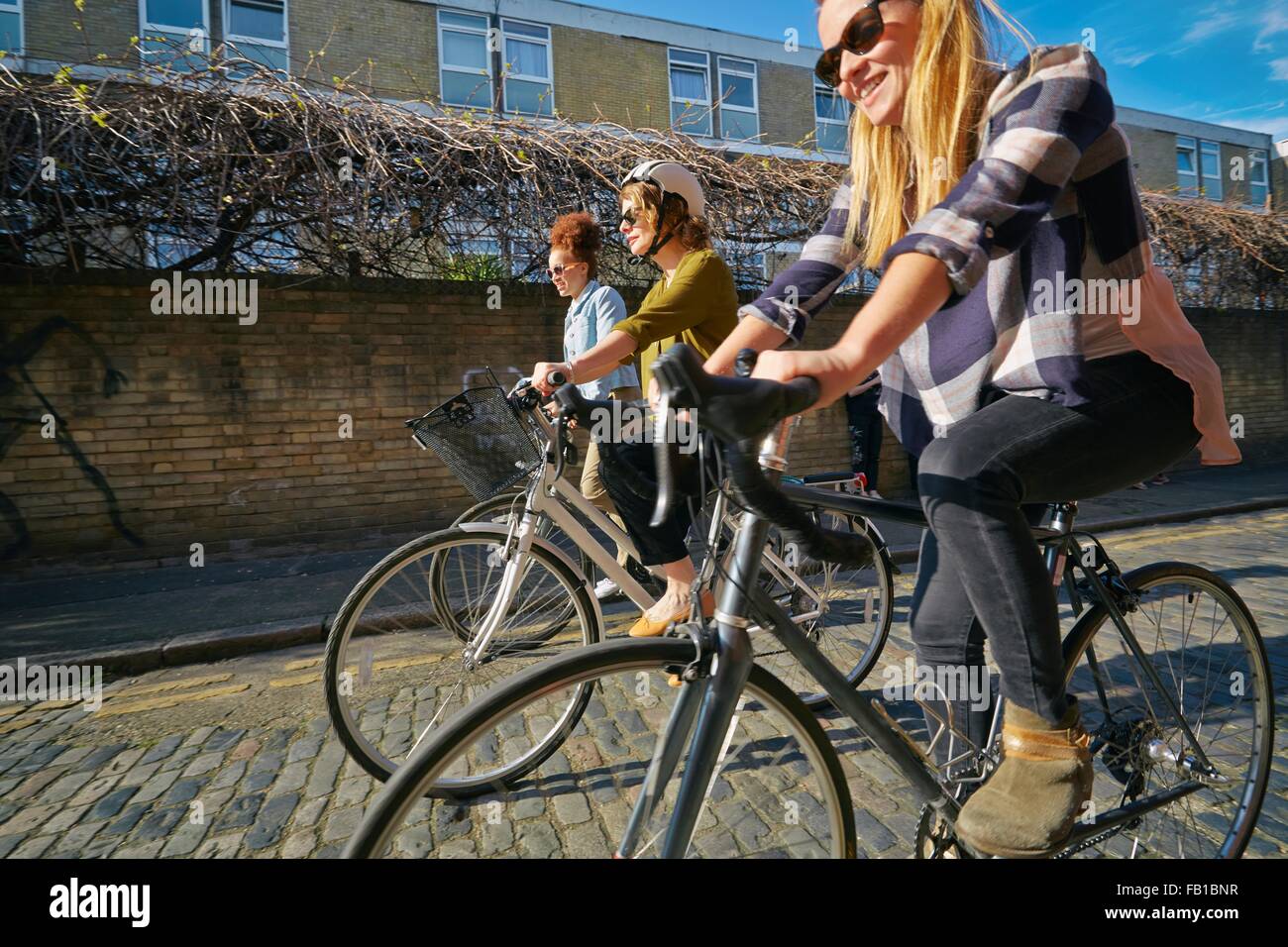 Side view of women cycling on bicycles on cobblestone road Stock Photo
