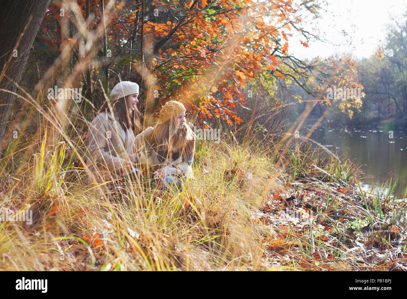 Teenage girls crouching on riverbank among tall grass looking away