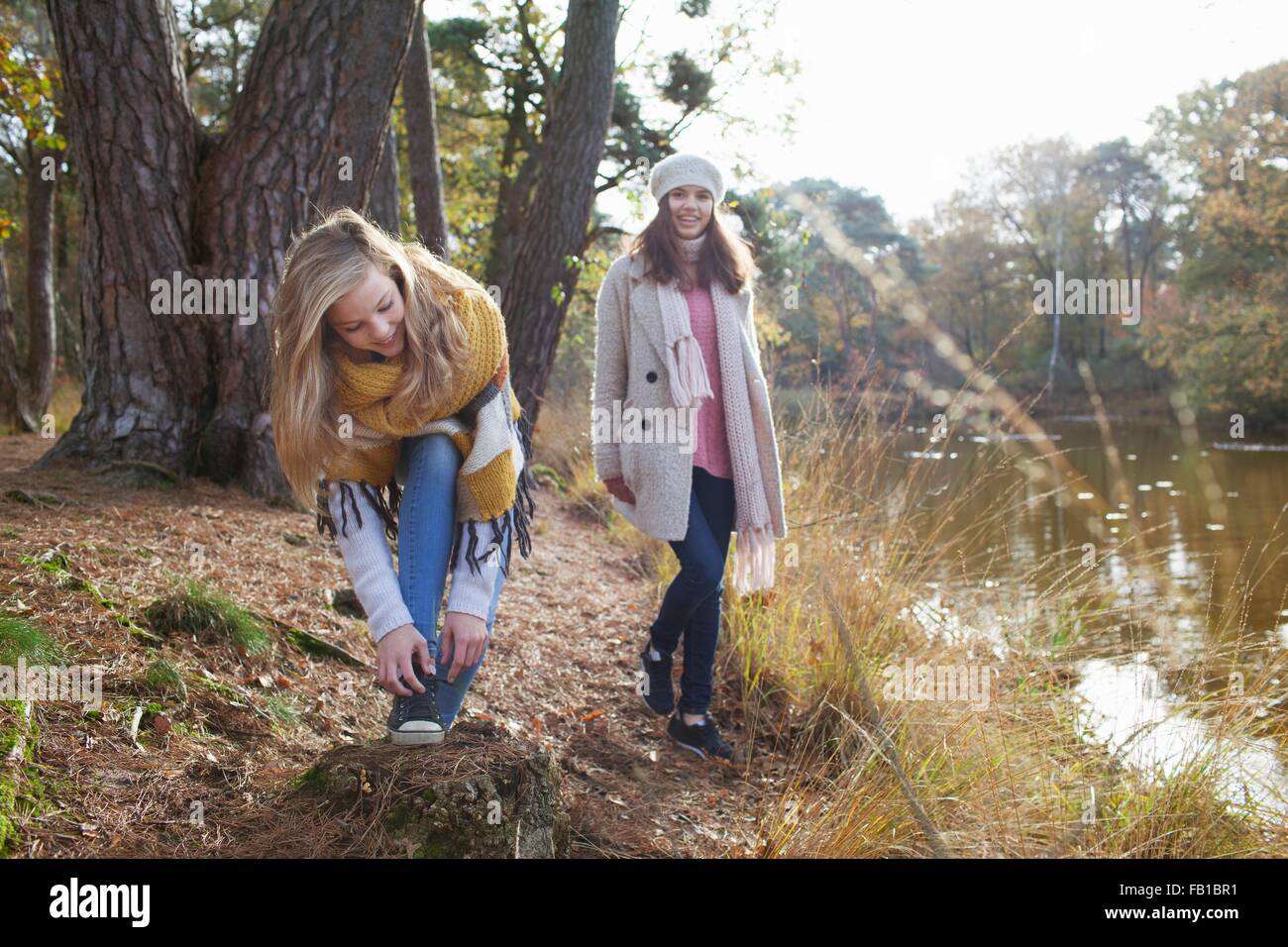 Teenage girls with friend on riverbank bending over tying shoelace Stock Photo