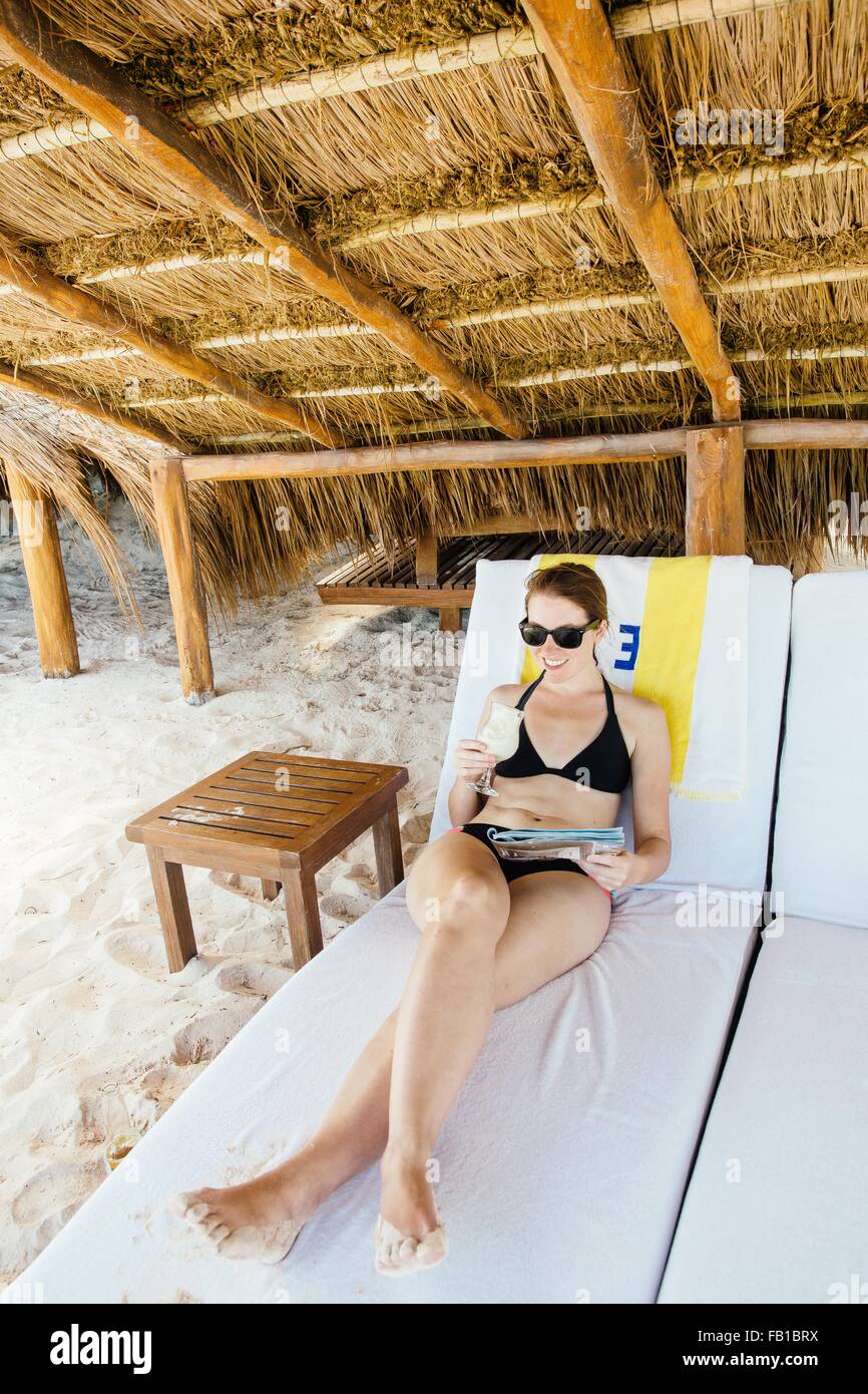 Mid adult woman relaxing on sun lounger, under cabana, Tulum, Riviera Maya, Mexico Stock Photo