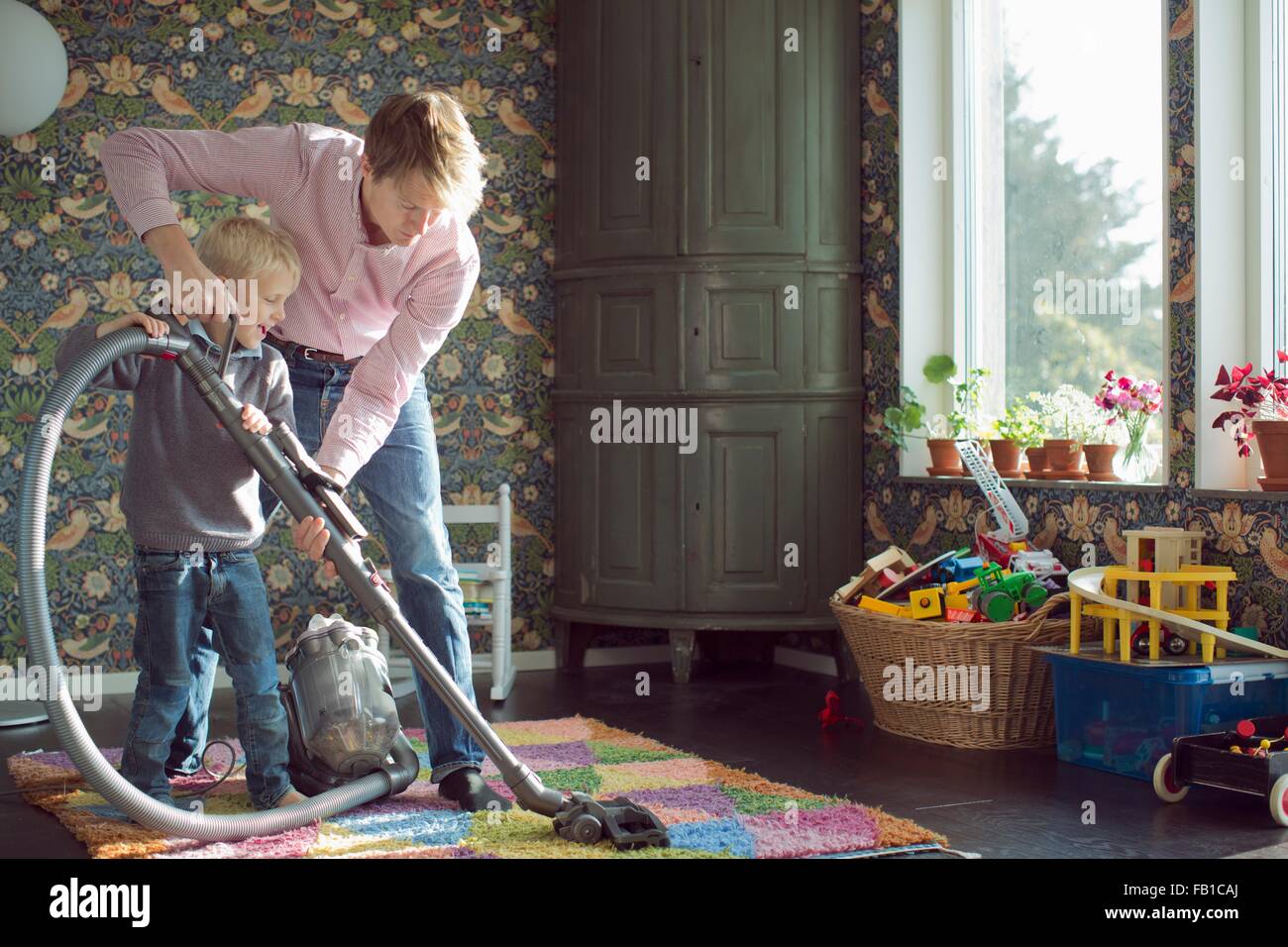Father and son vacuuming together in living Stock Photo