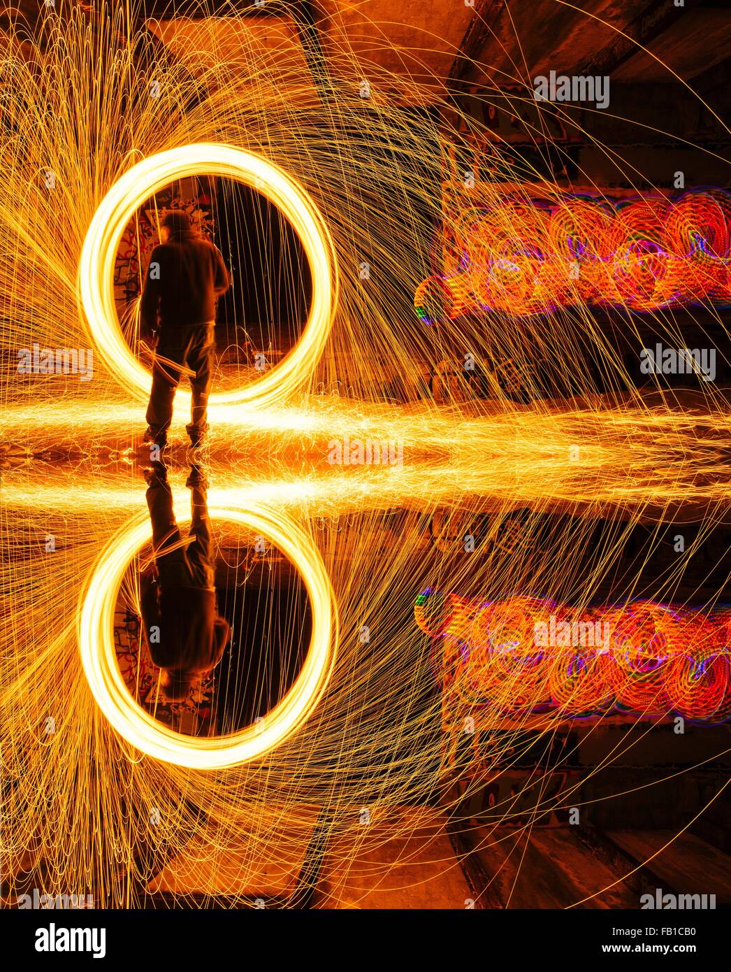 Mirror image of man creating circular golden spark light trails in derelict building Stock Photo