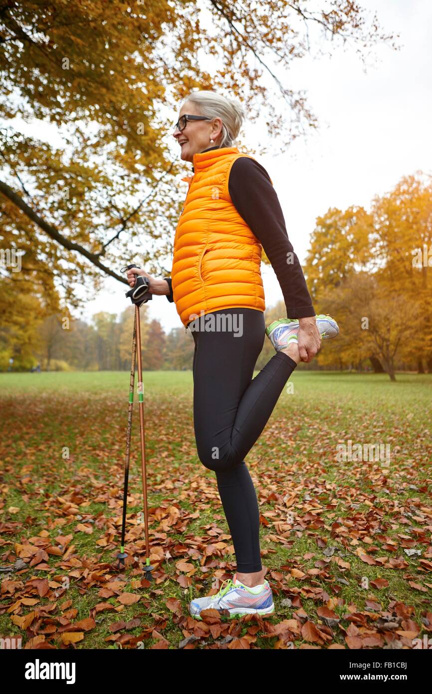 Senior female nordic walker standing on one leg in autumn park Stock Photo
