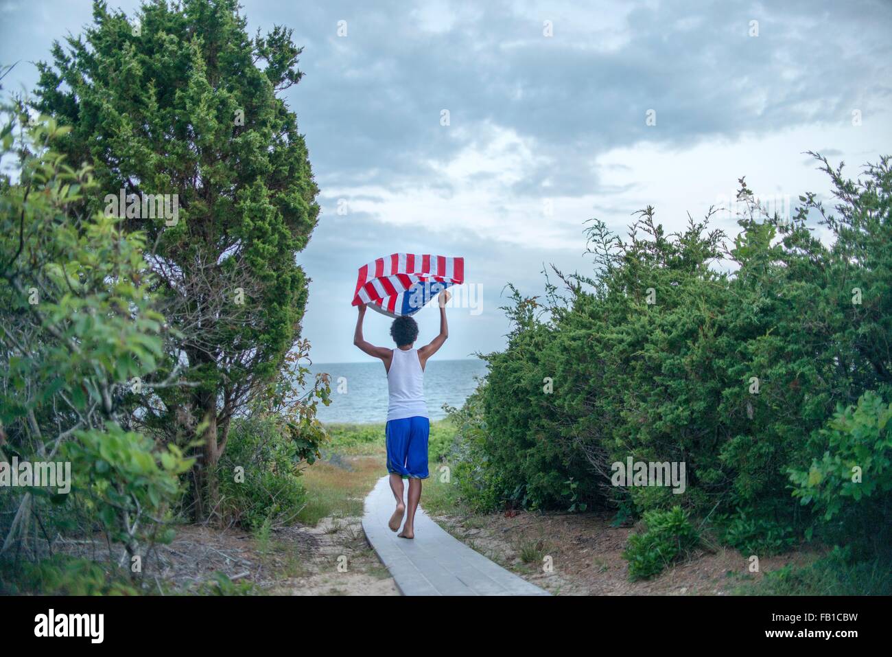 Rear view of boy holding up American flag on coastal path, Cape Cod, Massachusetts, USA Stock Photo
