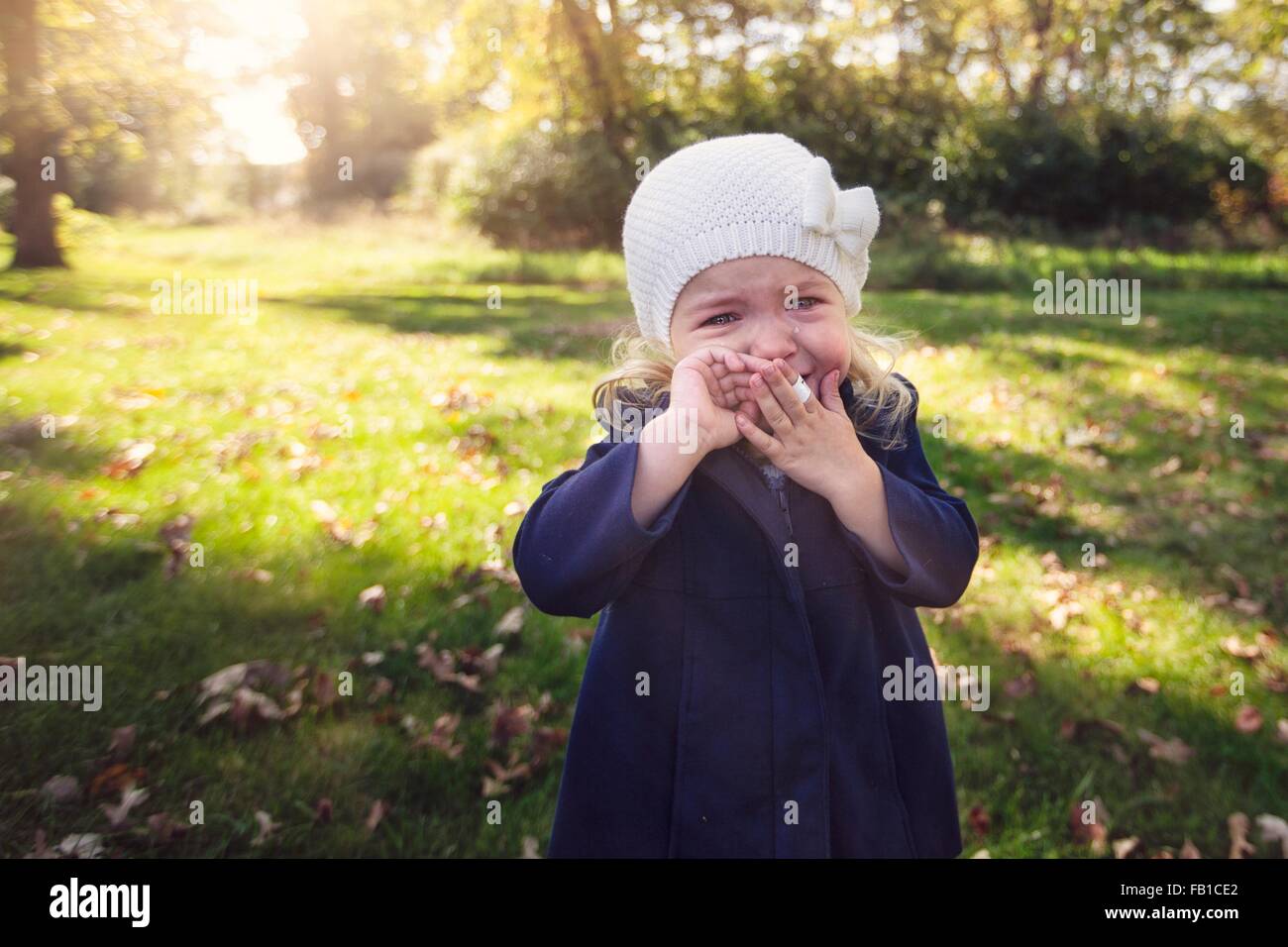 Girl wearing knit hat with adhesive plaster on finger hand to mouth crying Stock Photo
