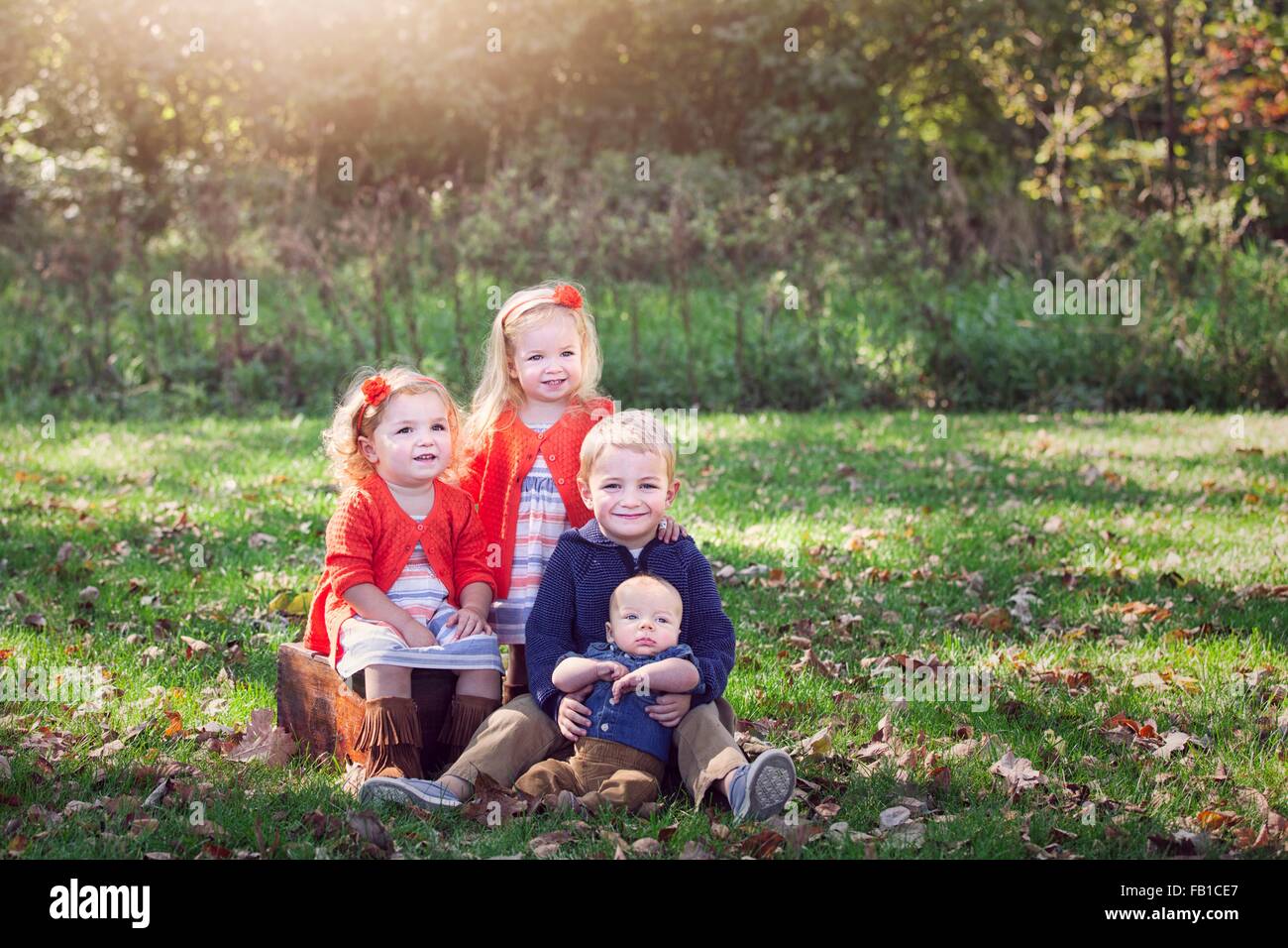 Four children family on autumn leaf covered grass posing for photograph smiling Stock Photo