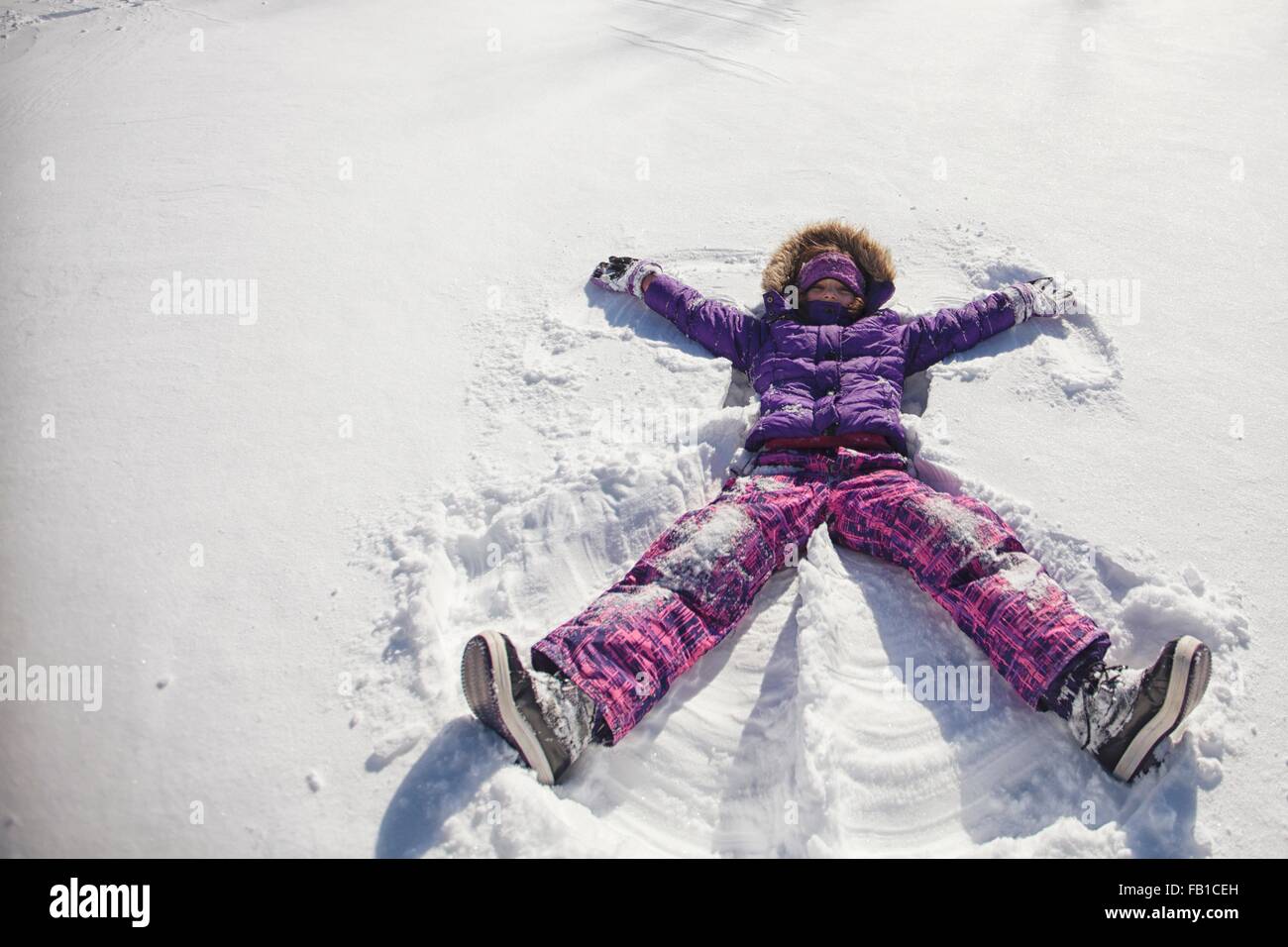 High angle view of girl wearing ski suit lying snow making snow angel Stock Photo