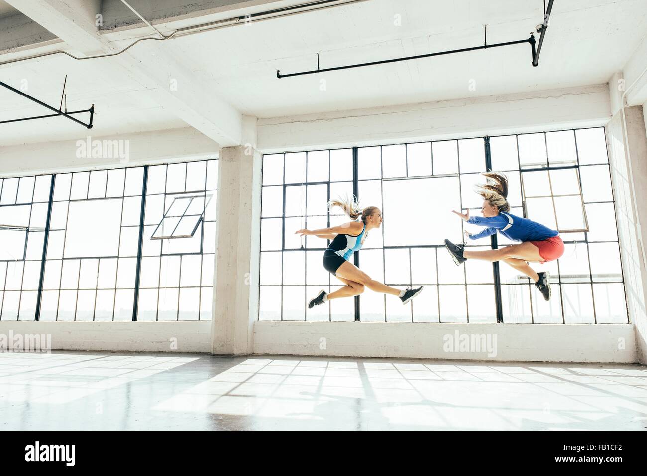Low angle side view of young women in gym doing mid air lunge Stock Photo