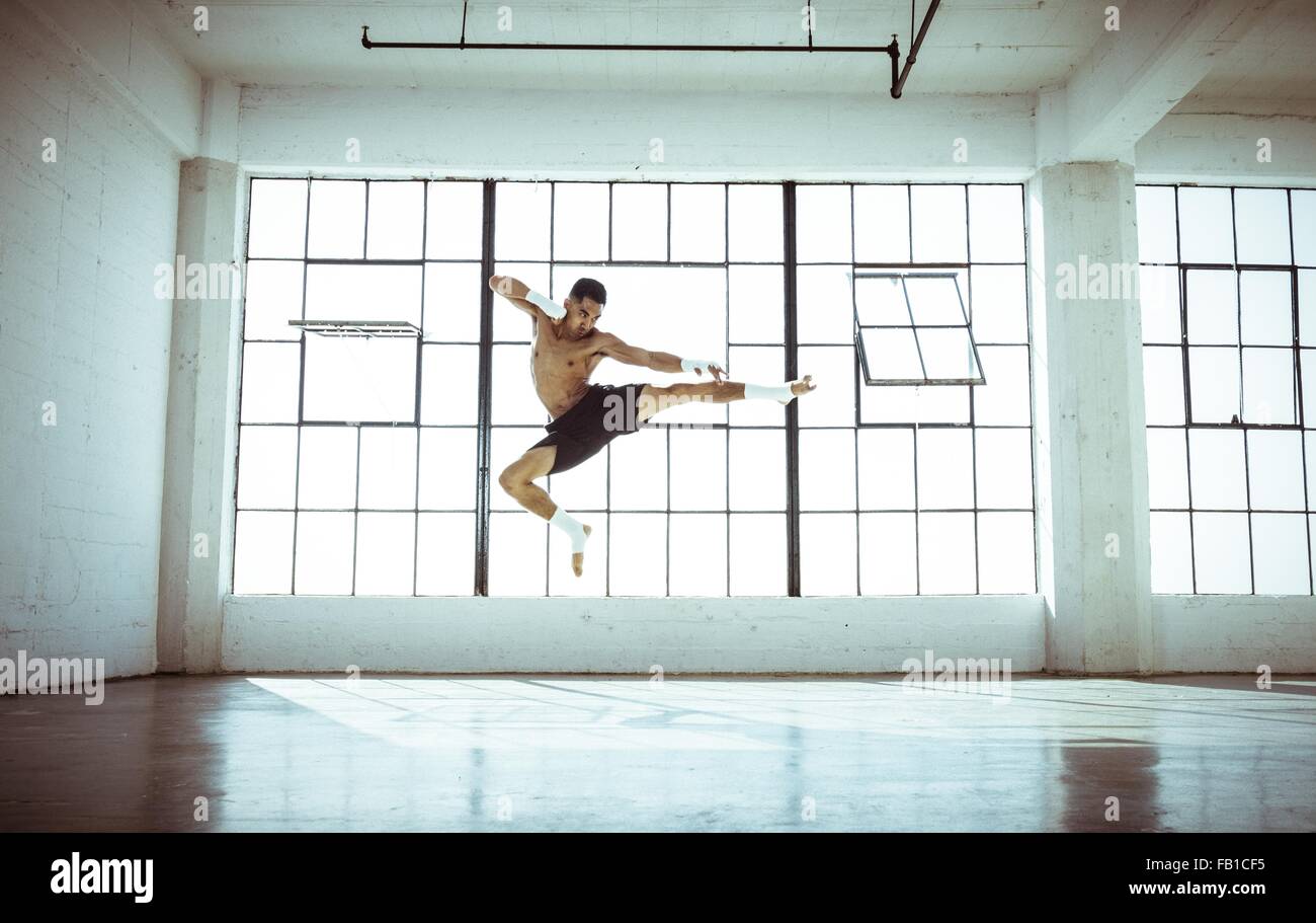 Full length front view of young man in gym in mid air kickboxing stance Stock Photo
