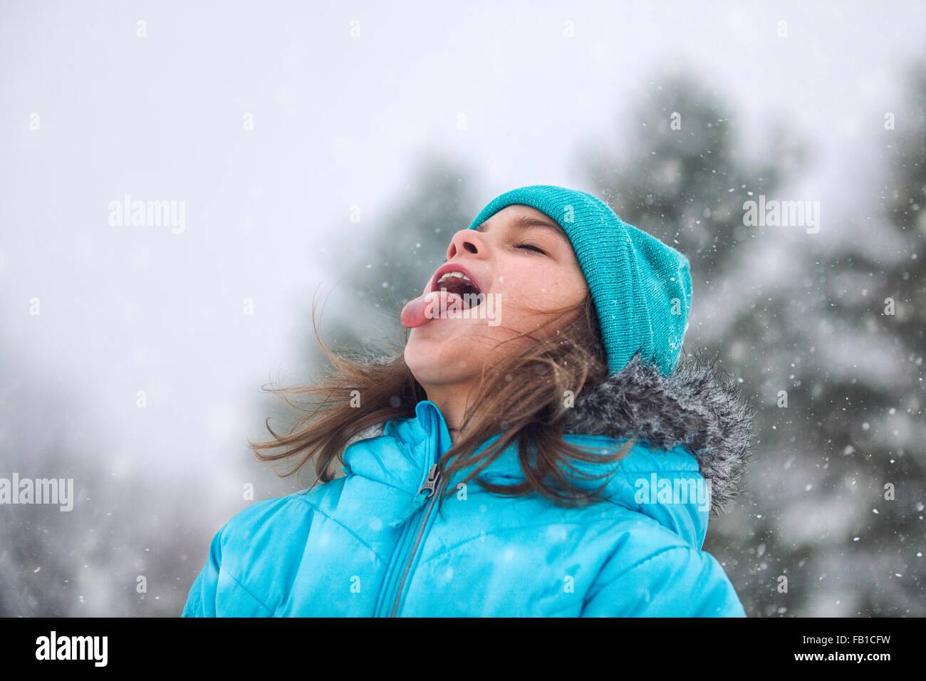 Girl looking up, sticking out tongue catching snowflakes Stock Photo