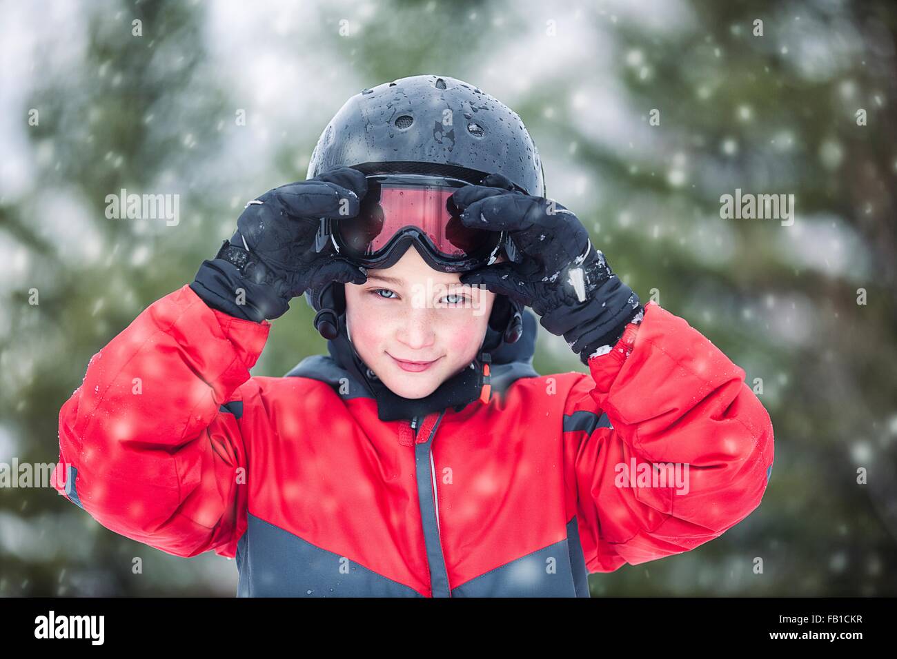 Boy wearing helmet and skiing goggles looking at camera smiling, snowing Stock Photo