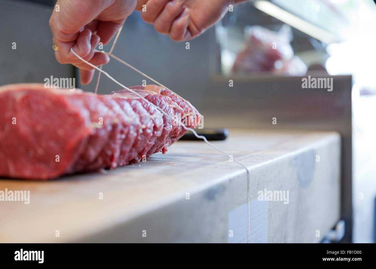 Close up of butchers hands tying meat joint on butchers block Stock Photo