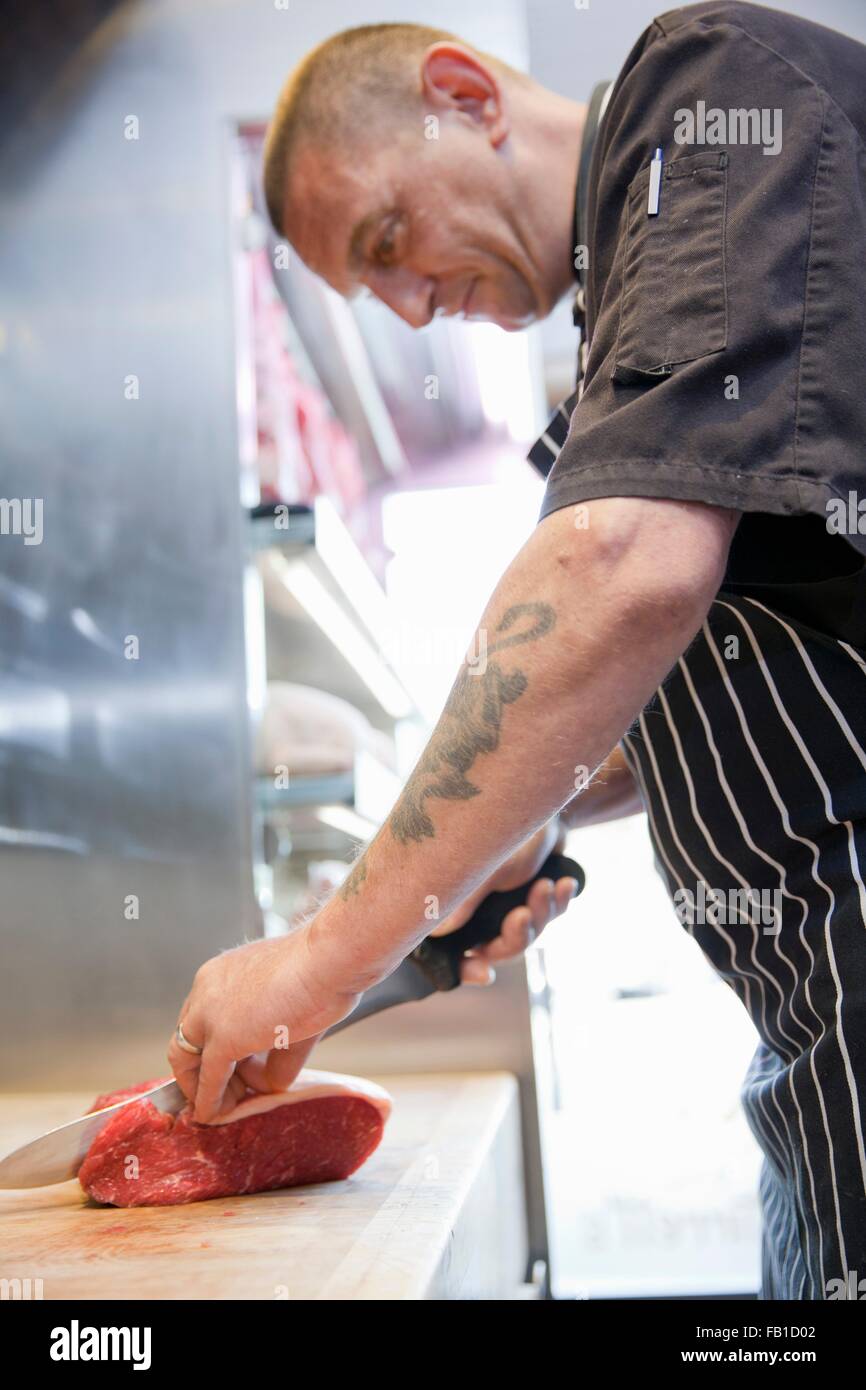 Mature butcher slicing raw steaks in butchers shop Stock Photo