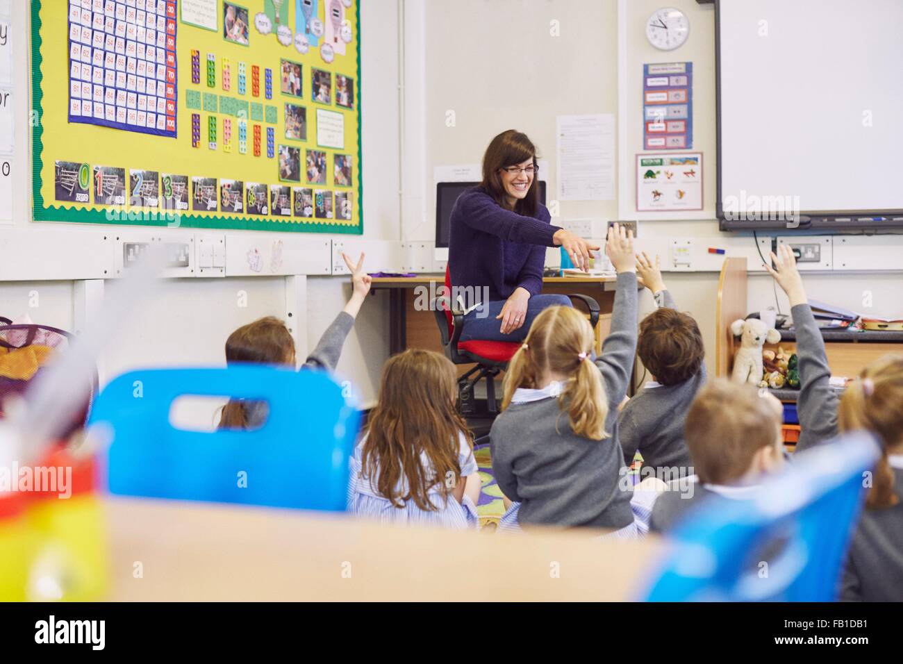 Teacher questioning children sitting on floor in elementary school classroom Stock Photo